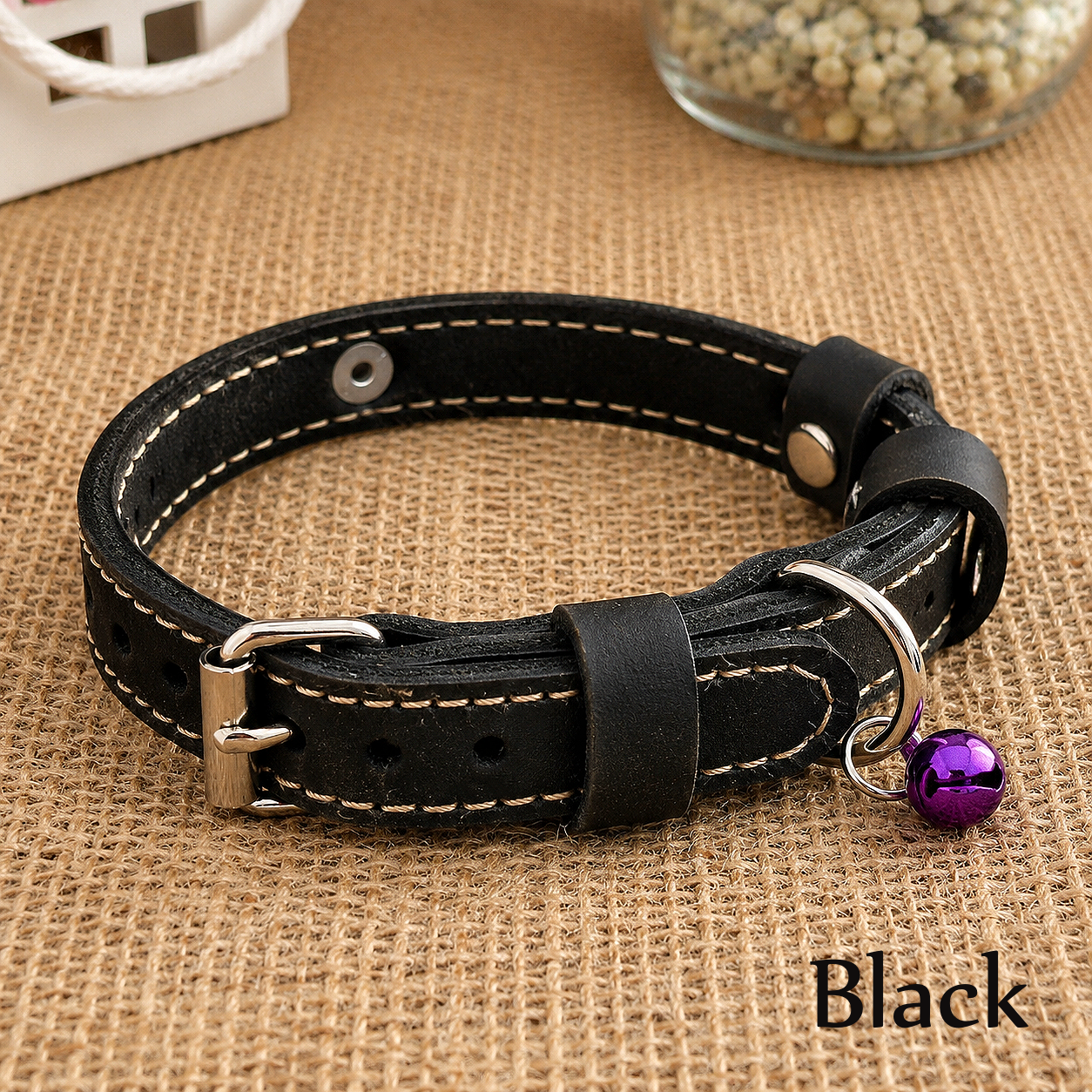 Black leather dog collar with a purple bell on a brown textured background