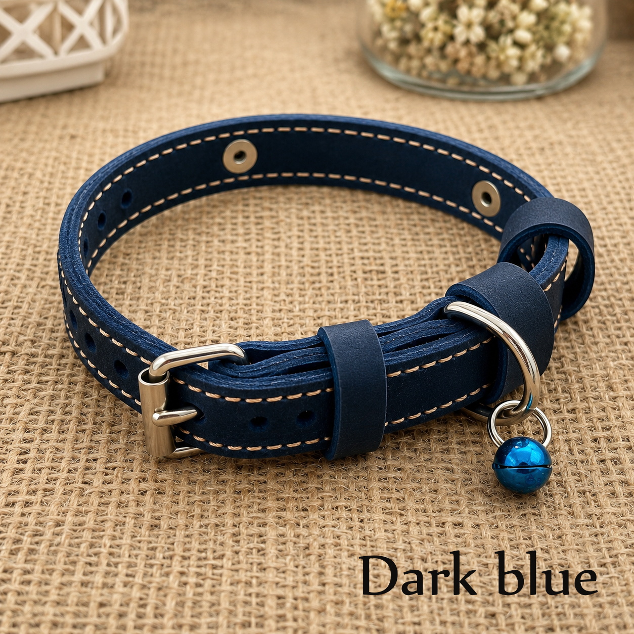 Dark blue-colored leather dog collar with a bell on a brown textured surface