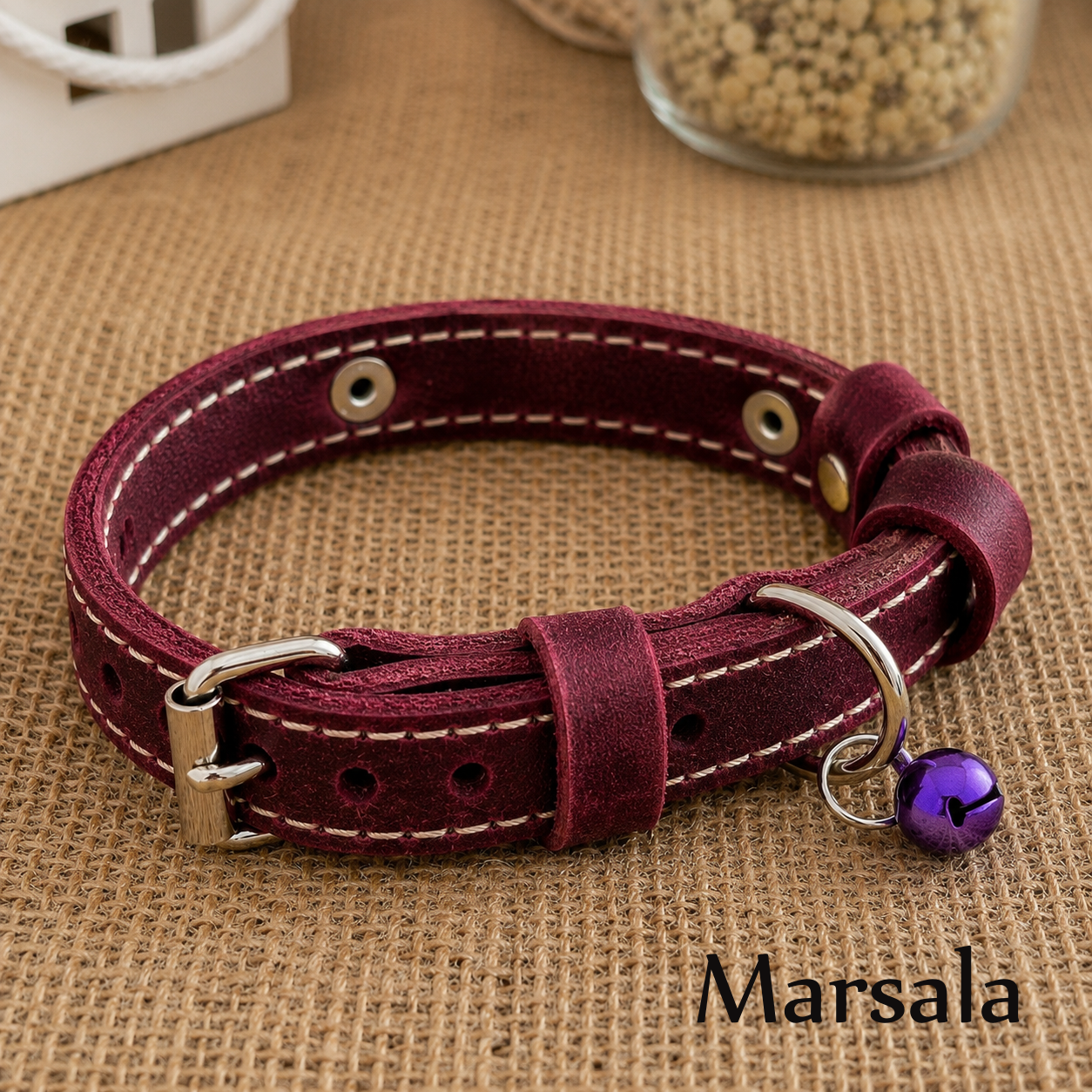 Maroon leather collar with a purple bell on a brown fabric background