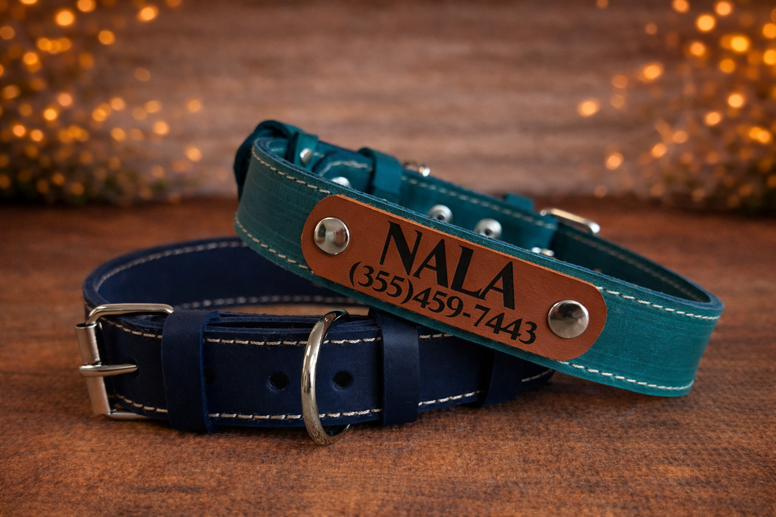 Two leather dog collars, one blue and one teal, with engraved names and phone numbers on a wooden surface.