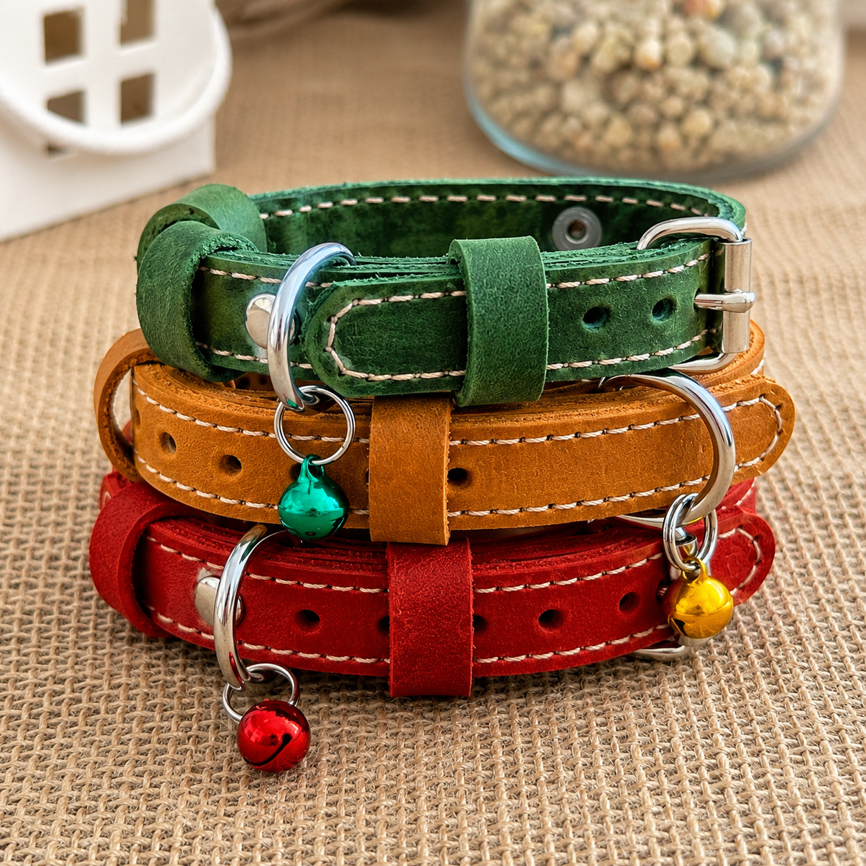 Three colorful leather dog collars stacked on a textured surface with small charms.