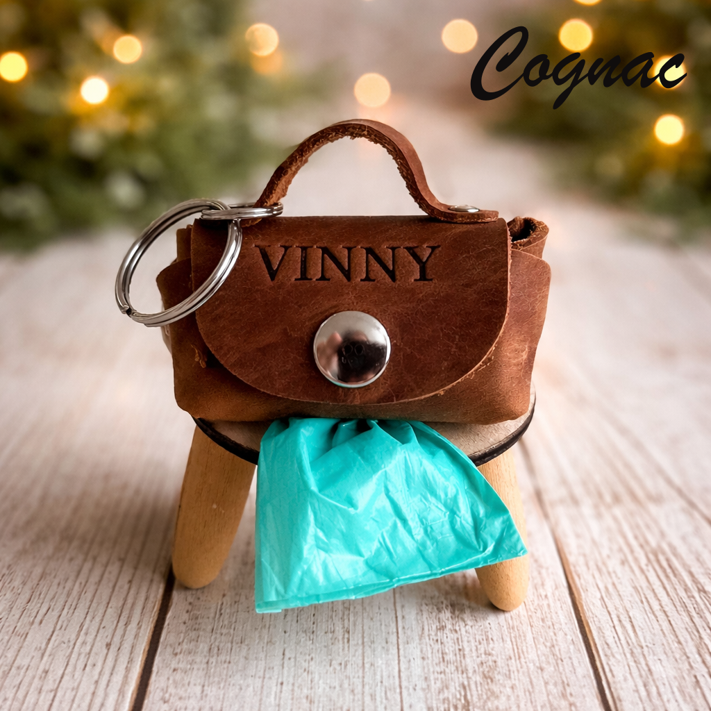 Brown leather keychain purse with 'VINNY' engraving on a wooden surface with blurred lights in the background.