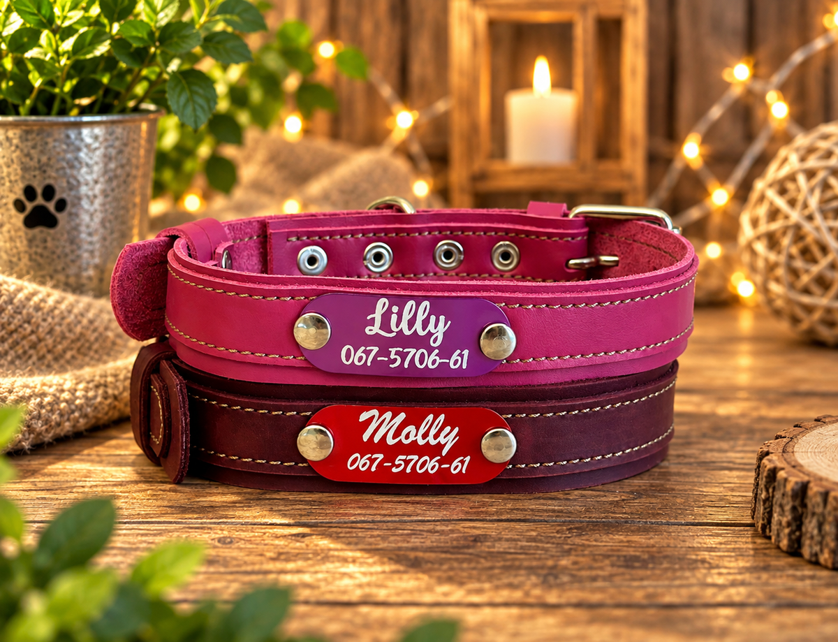 Two personalized leather dog collars stacked on a rustic wooden table. The top collar is a vibrant magenta pink with a purple oval plate engraved with 'Lilly 067-5706-61'.