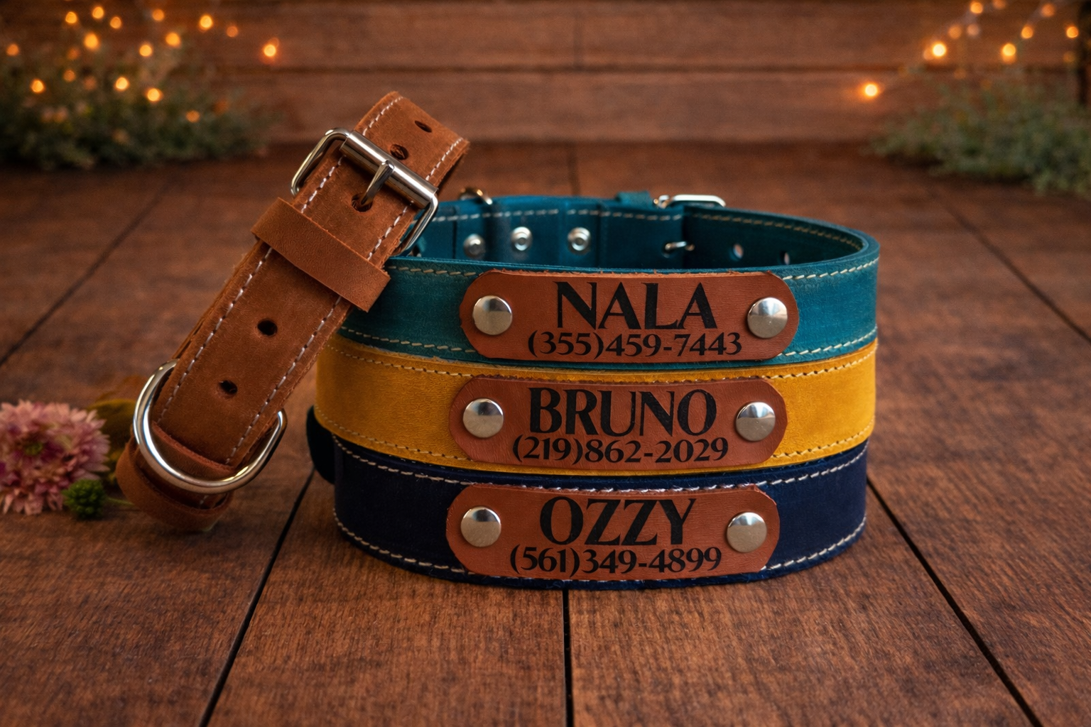 Three leather dog collars with engraved names and phone numbers on a wooden surface.