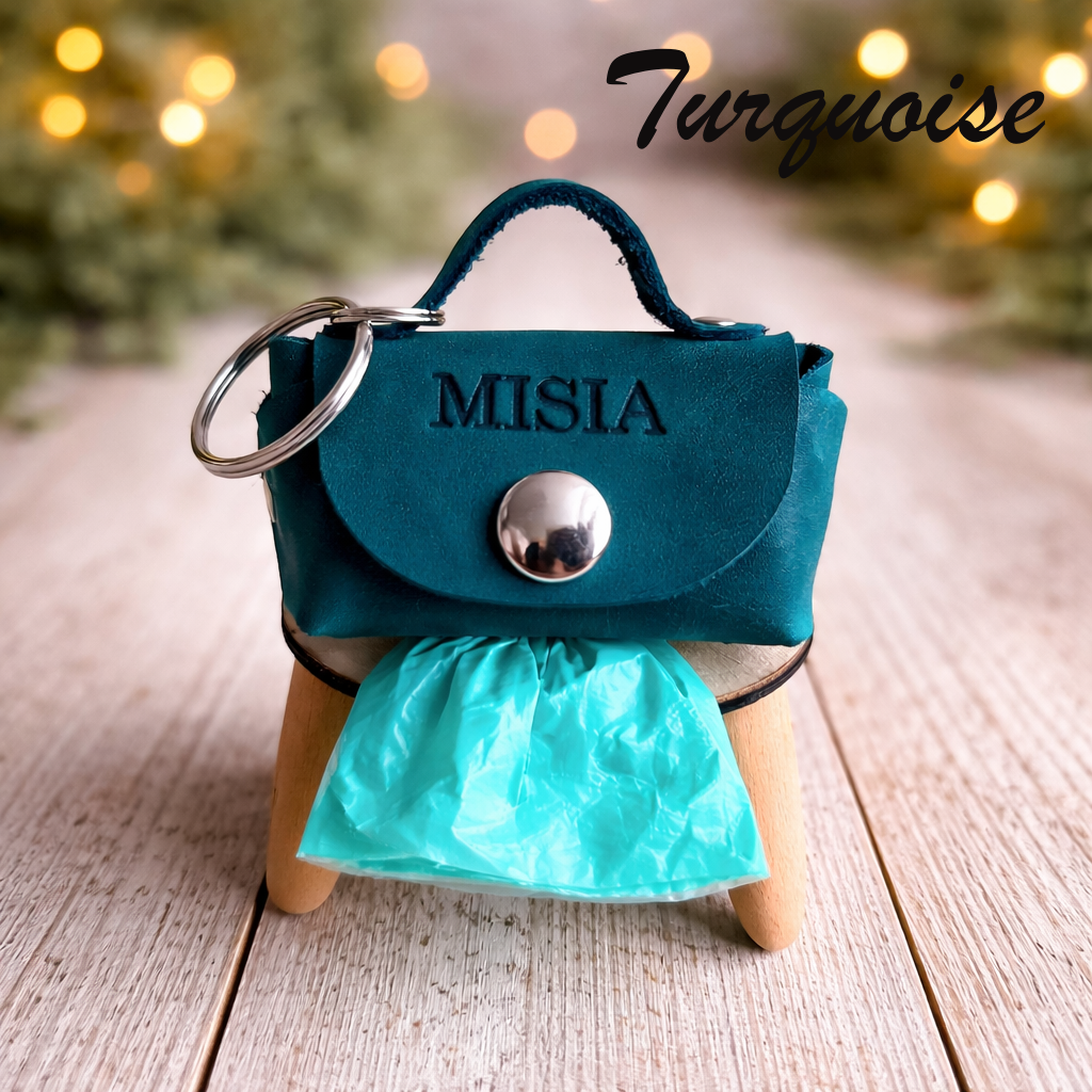 Turquoise handbag-shaped keychain with 'MISIA' branding on a wooden surface.