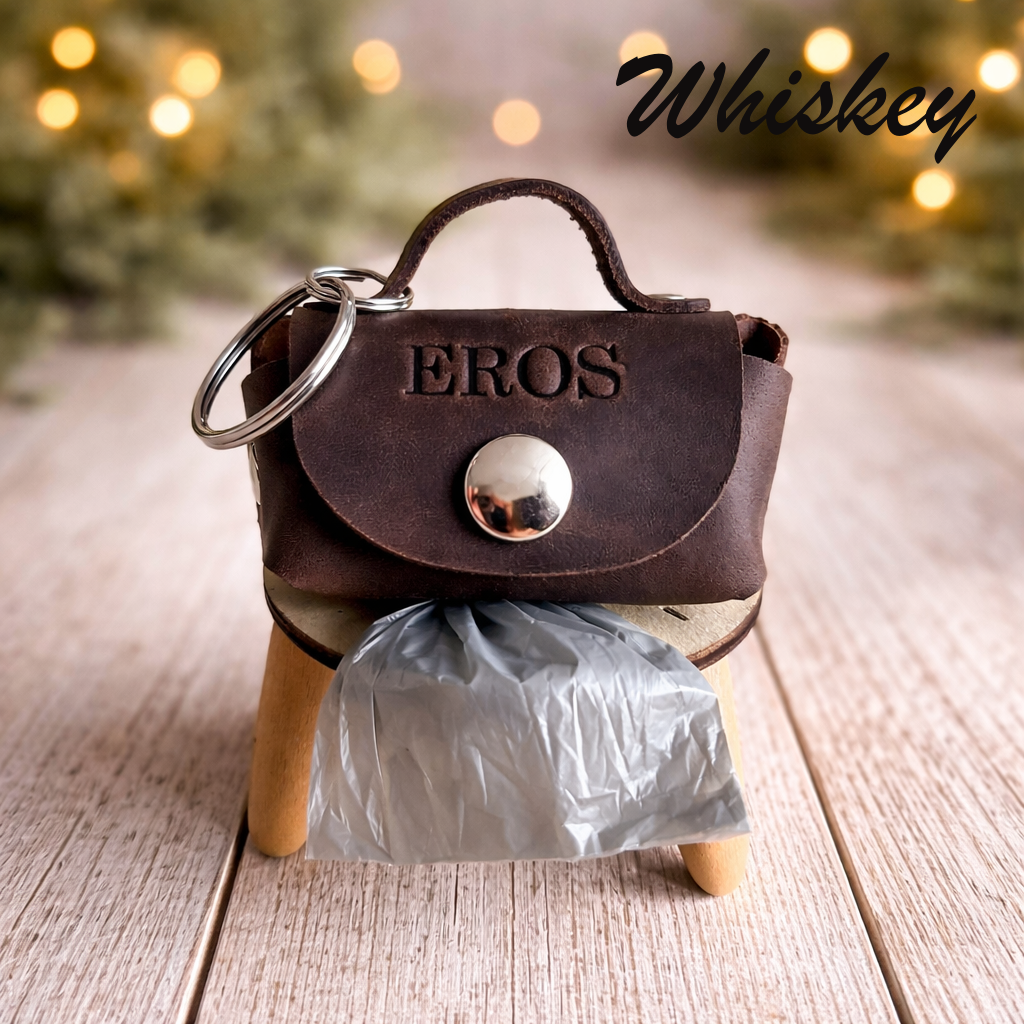 Brown leather keychain purse with 'EROS' branding on a wooden stand with blurred lights in the background.