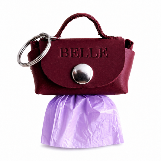 Maroon handbag-shaped keychain with 'BELLE' branding and a purple skirt on a white background