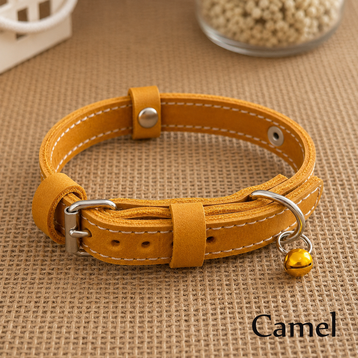 Camel-colored leather dog collar with a bell on a brown textured surface