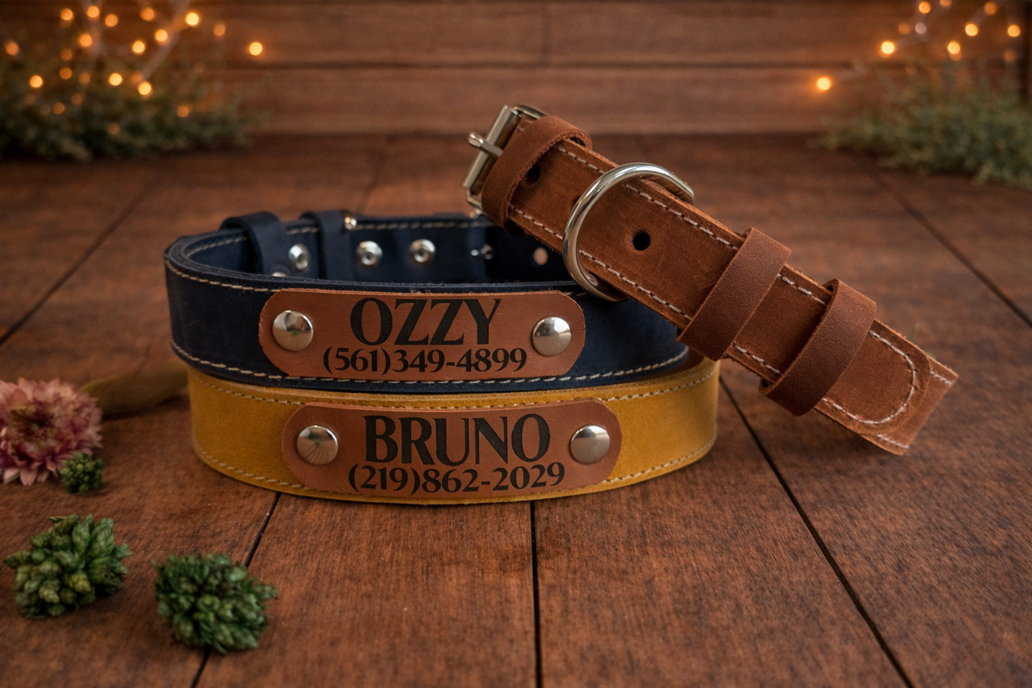 Two leather dog collars with engraved names and phone numbers on a wooden surface.