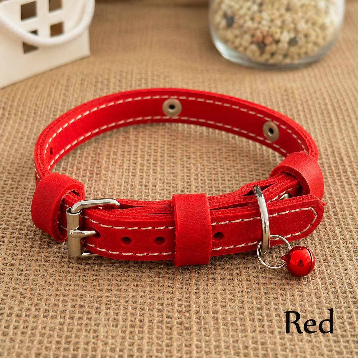 Red leather dog collar with a bell on a brown textured surface