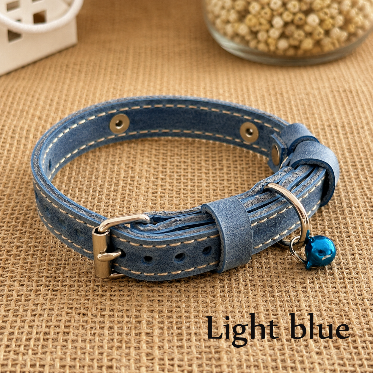 Light blue leather dog collar with a metal buckle and blue tag on a brown fabric background.