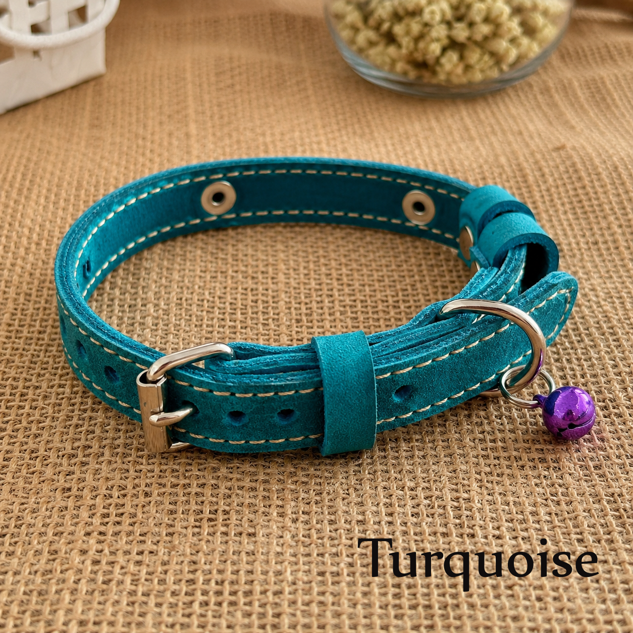 Turquoise leather dog collar with a purple bell on a brown fabric background