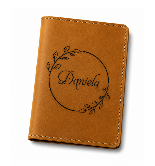 A tan leather passport cover with a circular leaf wreath design and the name 'Daniela' printed in the center, shown on a clean white background.