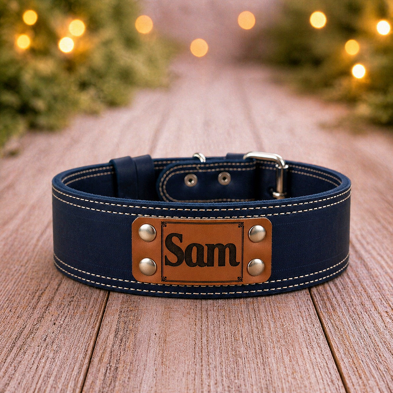 Navy leather dog collar with a brown nameplate on a wooden surface, Christmas lights in the background.