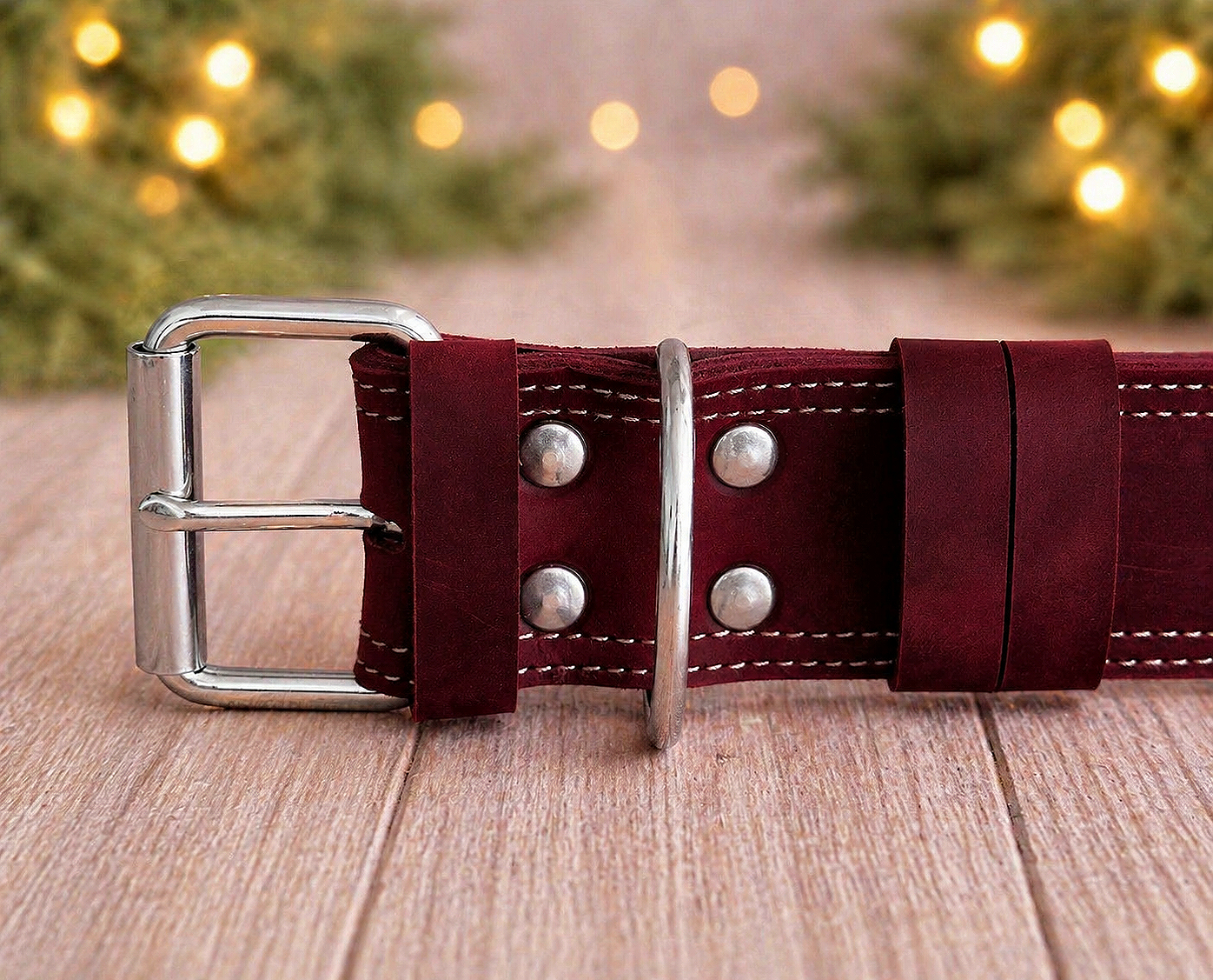 Maroon leather belt with silver buckle on a wooden surface with blurred lights in the background
