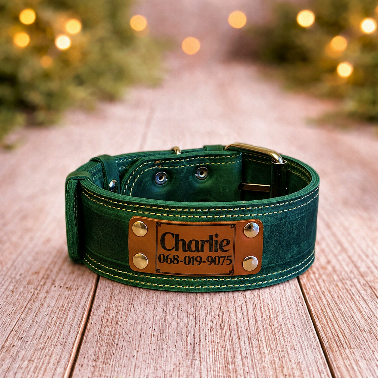 Green leather dog collar with a nameplate on a wooden surface, blurred Christmas lights in the background.