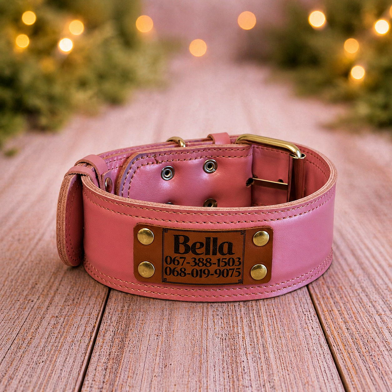 Pink leather dog collar with brass hardware on a wooden surface, blurred lights in the background