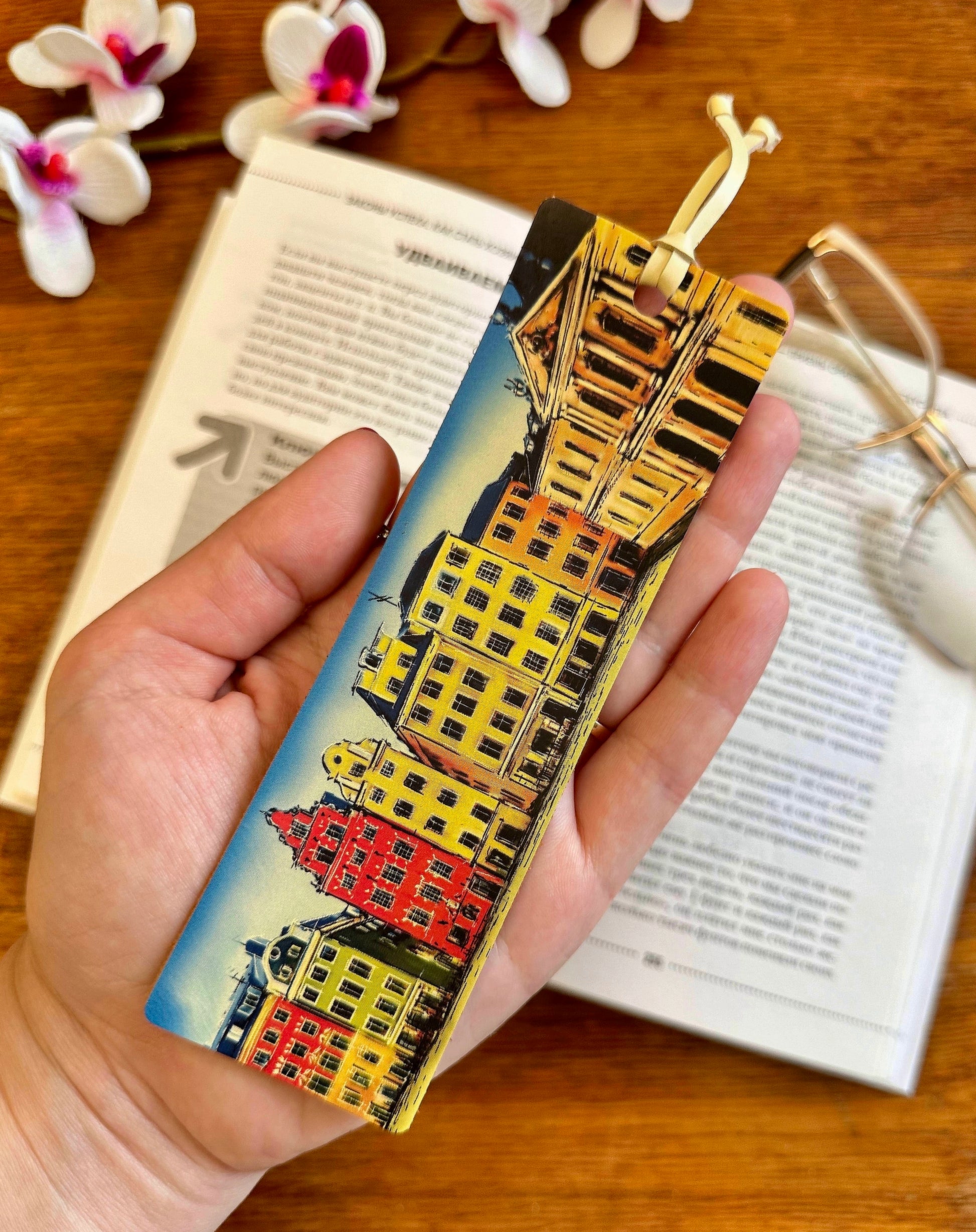 Leather bookmark with floral print, placed next to a candle and coffee cup, creating a cozy reading atmosphere
