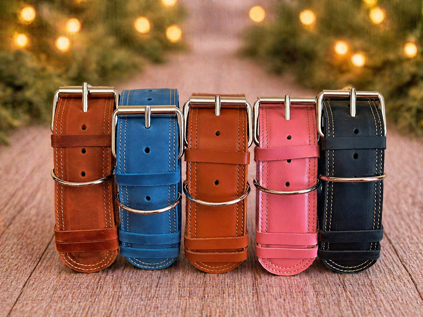 Five leather watch straps in brown, blue, red, pink, and black on a wooden surface with blurred Christmas lights in the background.