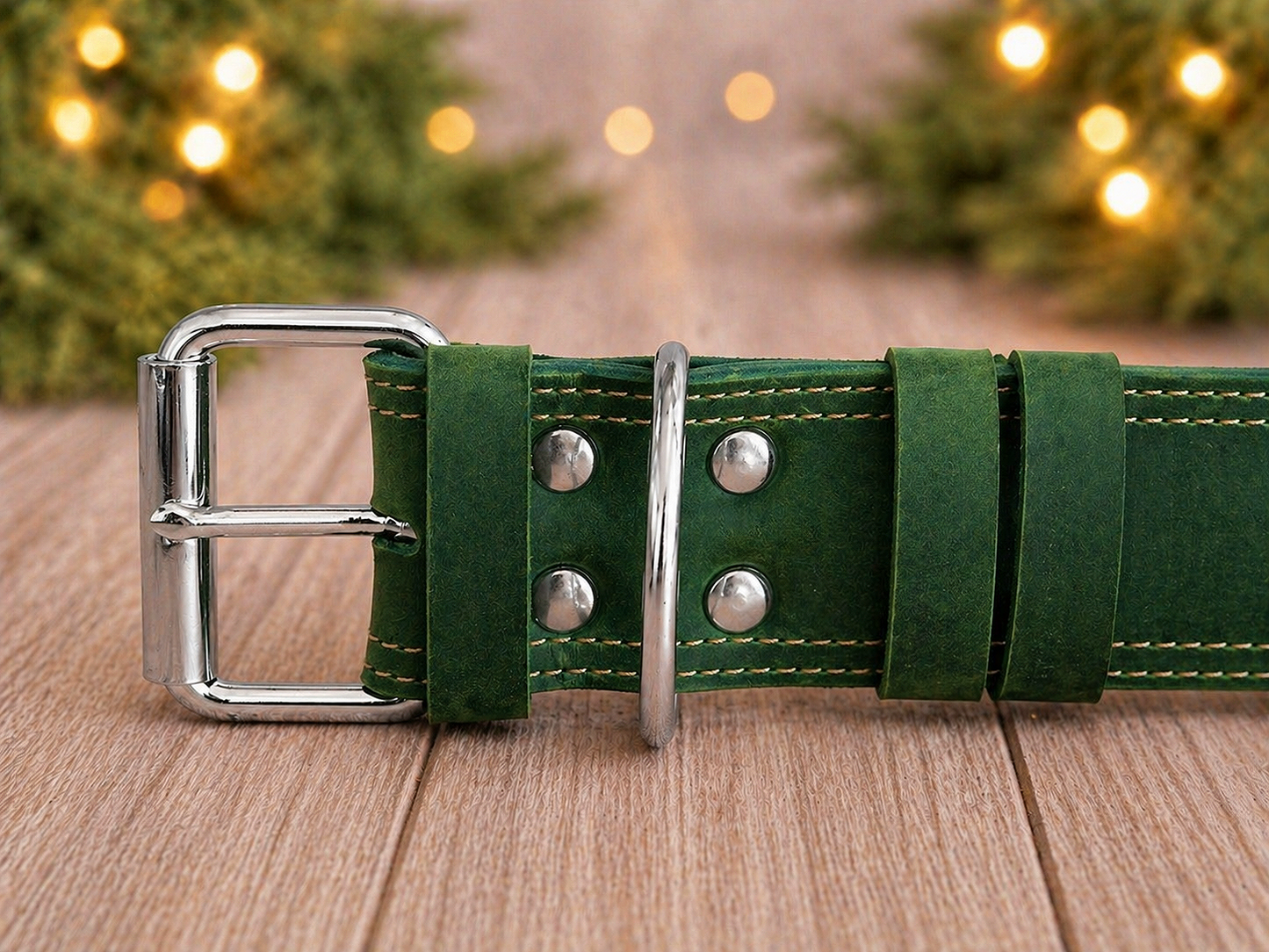Green leather belt with silver buckle on a wooden surface with blurred Christmas lights in the background